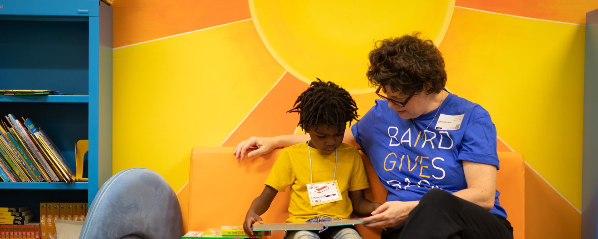 Woman in a Nexus Cares t-shirt reading to a student.