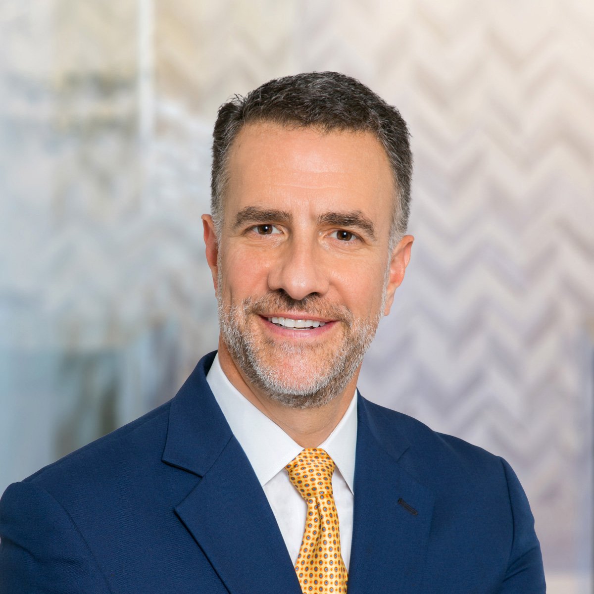 Professional headshot of Chris Cooper wearing a blue suit and a gold tie.