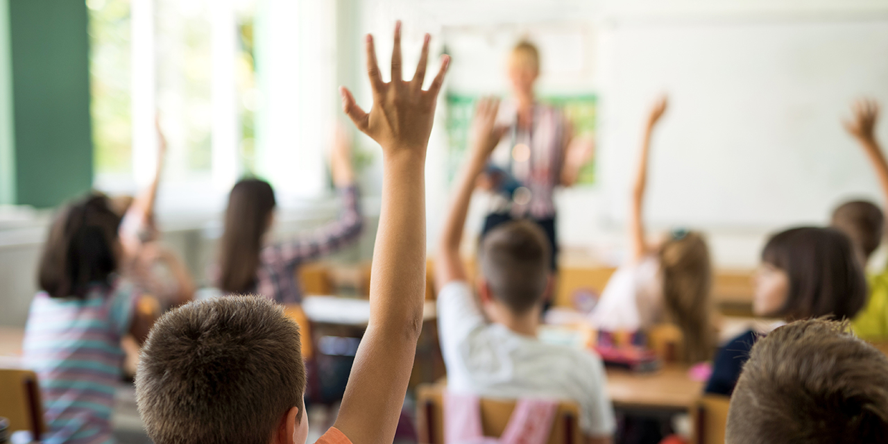 School children in a classroom with hands raised.