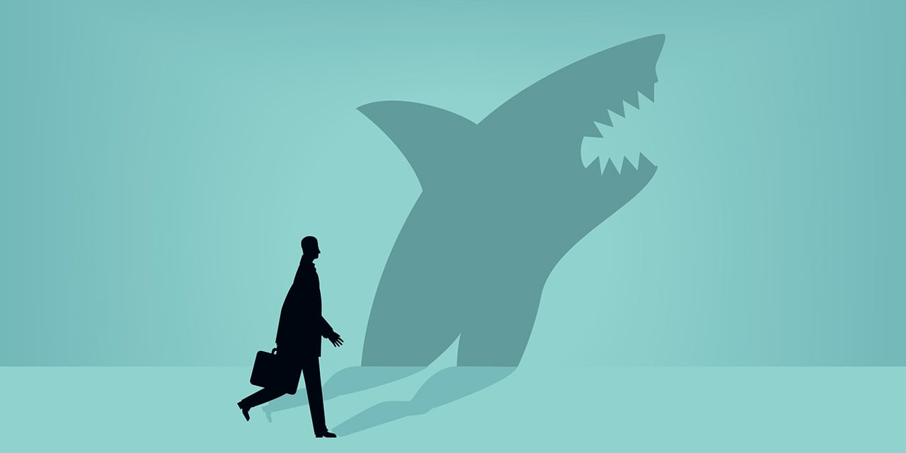 Shadow of a shark on a wall with a figure of a person walking in front of the wall.