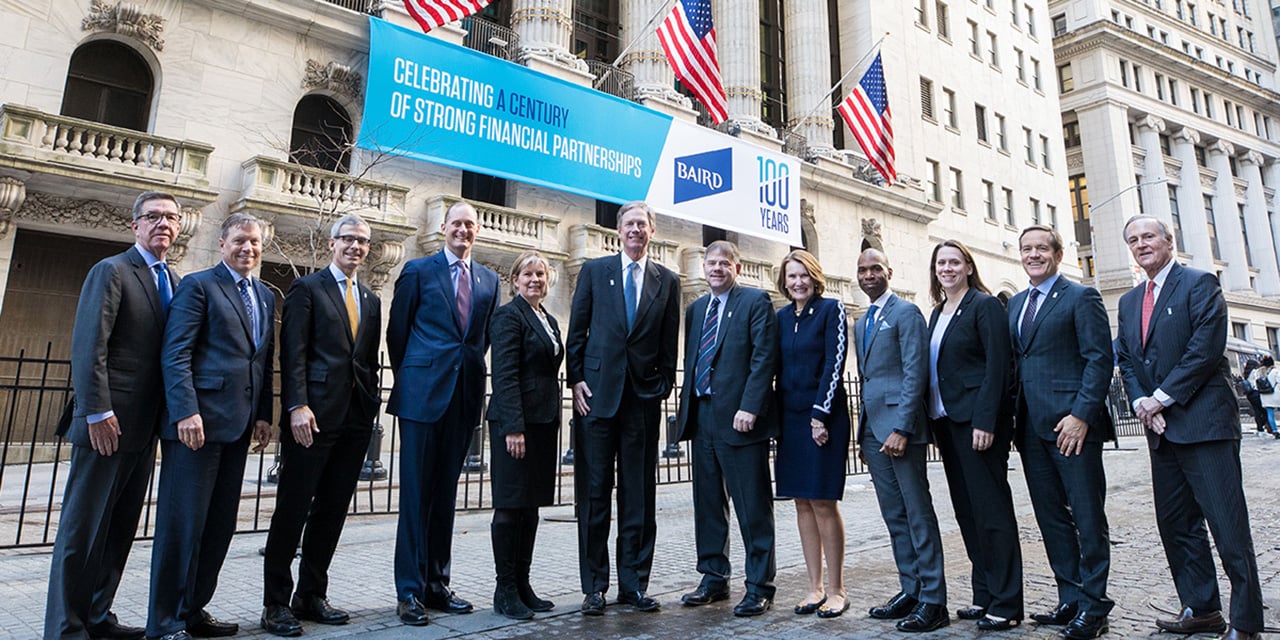  Nexus leadership standing in front of the New York Stock Exchange with a banner celebrating Nexus 's 100th anniversary in the background.